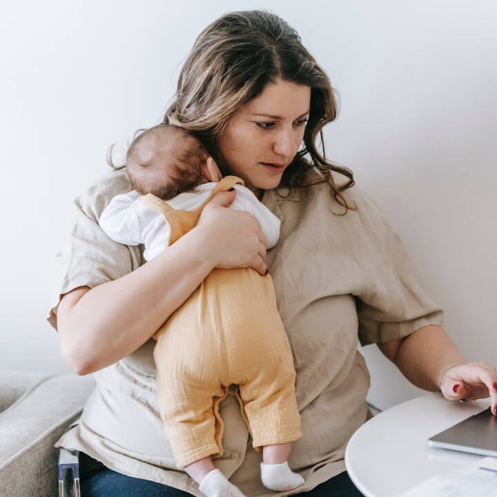 mother holding baby while working on laptop