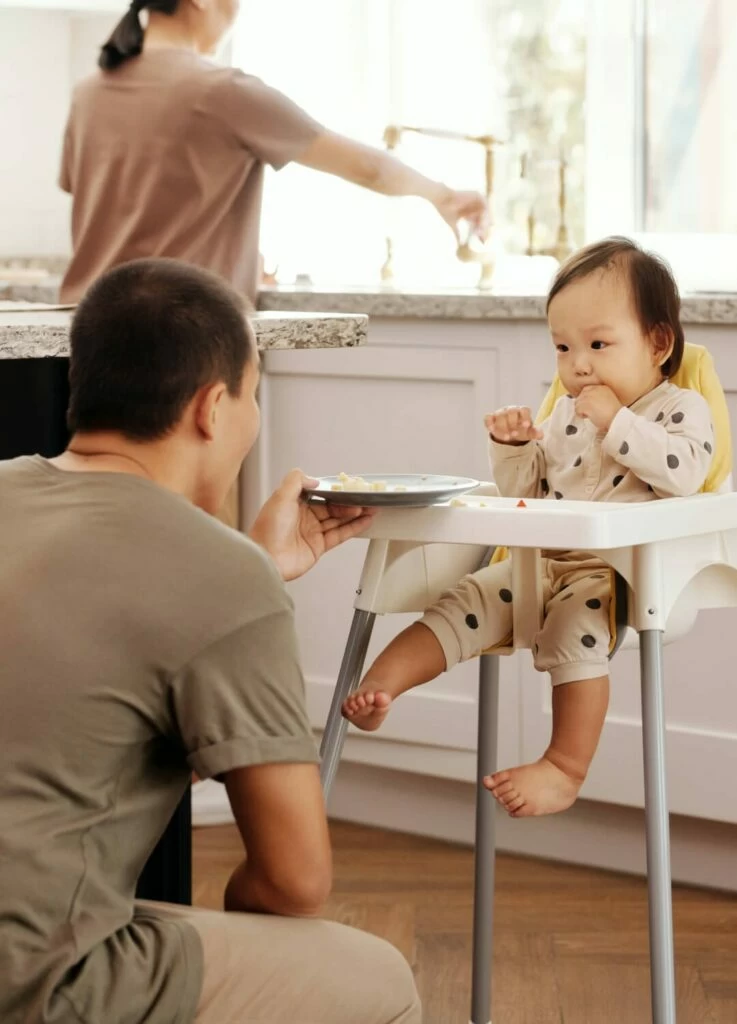father feeding baby in high chair